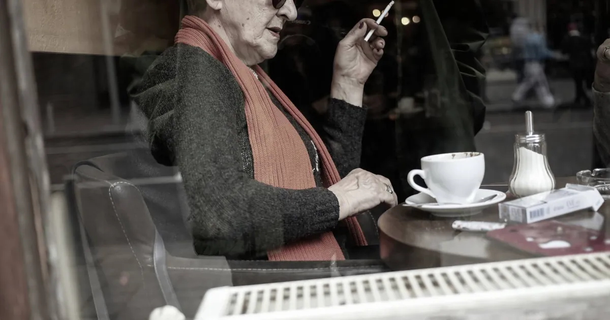 Une cliente qui fume à la fenêtre d'un café, tasse posée devant elle